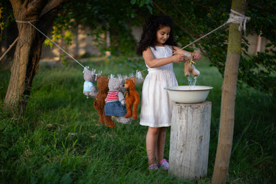 Enfant qui lave ses doudous et peluches dans une bassine à l'extérieur