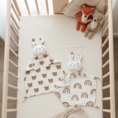 Doudou lapin en arc-en-ciel et ourson déposé sur lit 