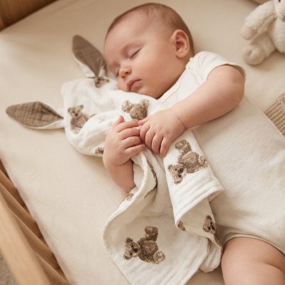 Doudou ourson assis tenu par un nourrisson endormi sur le dos