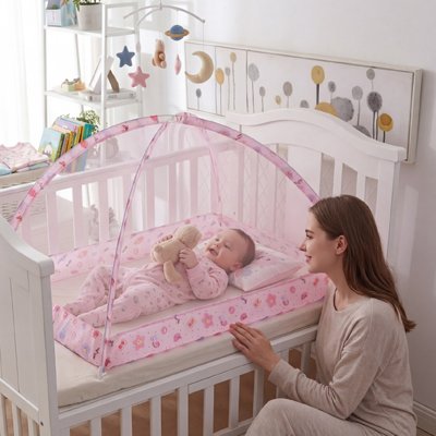 Moustiquaire pour lit bébé dépliée au dessus d'un nourrisson joyeux